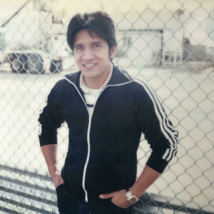 Man in retro tracksuit embodying 60s fashion looks, standing in front of a chain-link fence, smiling confidently.