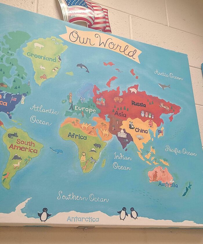 World map in a US school classroom displaying continents and oceans, with an American flag above.