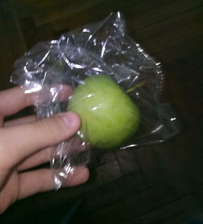 A hand holding a green apple wrapped in plastic, representing a common school experience item.