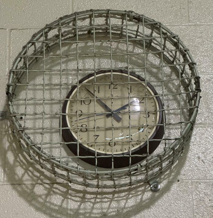 A wall clock covered with a metal cage in a school hallway, illustrating horrifying school experiences.