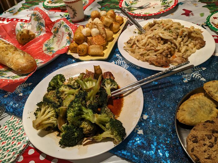 Festive Christmas dinner table with various dishes, including broccoli and pastries, set on a colorful tablecloth.
