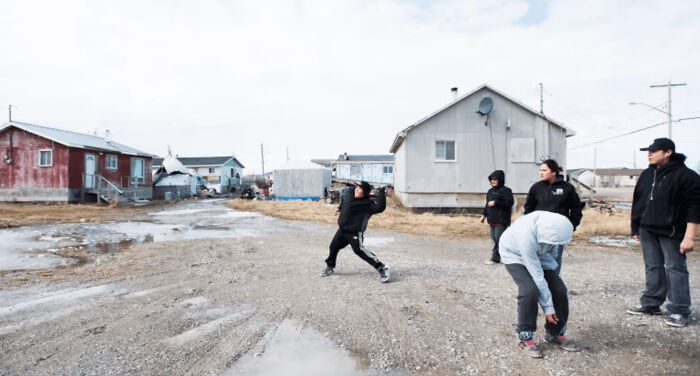 Group of people in a rural area with unpaved road, highlighting an urban hell scene with isolated houses and cloudy sky.