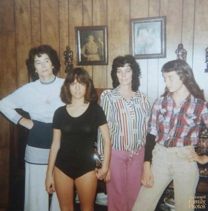 Awkward family photo with four people posing in a room with wood paneling and framed pictures.