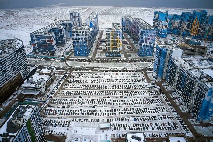 Urban hellscape with snow-covered high-rise buildings and packed parking lot, showcasing bleak city architecture.
