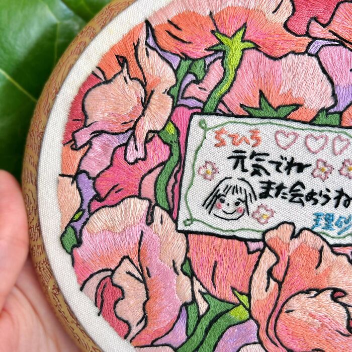 Hand holding embroidery hoop with colorful floral embroidery and a stitched message in the center, showcasing beautiful embroidery designs.