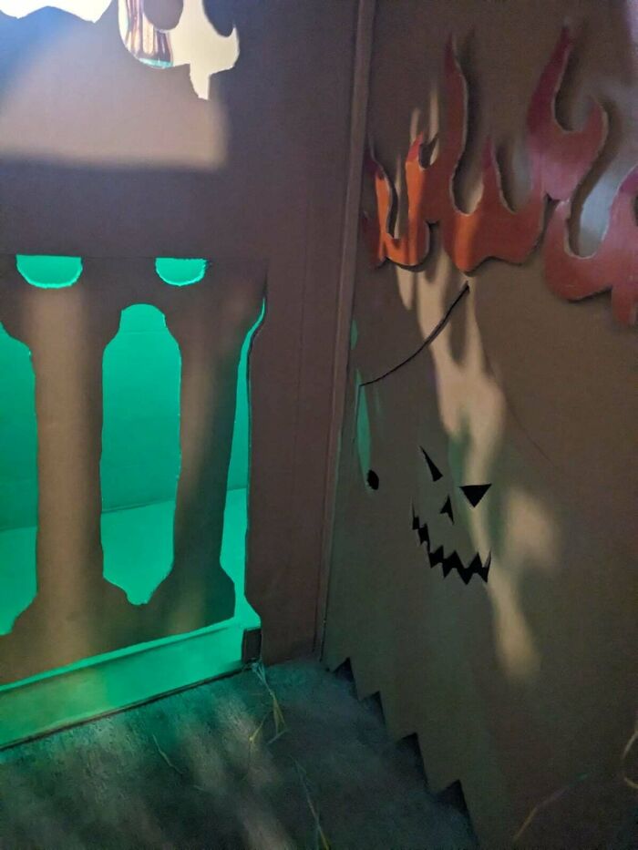 Cardboard decoration with green glow depicting flames and a jack-o-lantern face, reflecting consumerism effects.