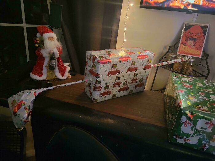 Hilarious trolling Christmas gift with funny-shaped wrapping, displayed on a table with Santa decoration nearby.