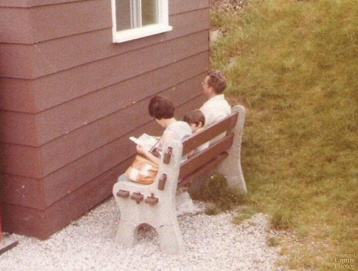 Awkward family photo with people sitting on a bench facing the wall of a house.