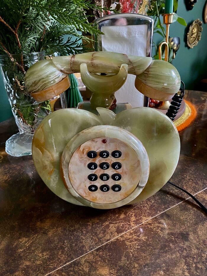 Vintage green onyx rotary phone thrifted, placed on a wooden table with plants in the background.