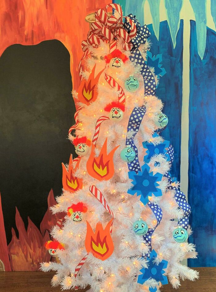 White Christmas tree decorated with flame and snowflake motifs, adorned with colorful ribbons and cartoon face ornaments.