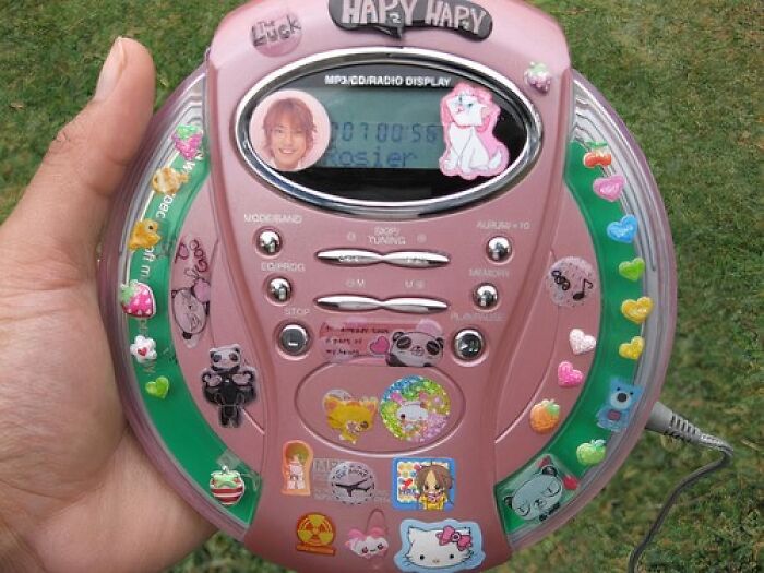 Old-Internet-Feel-Pics: Hand holding a vintage pink portable CD player covered in colorful stickers.