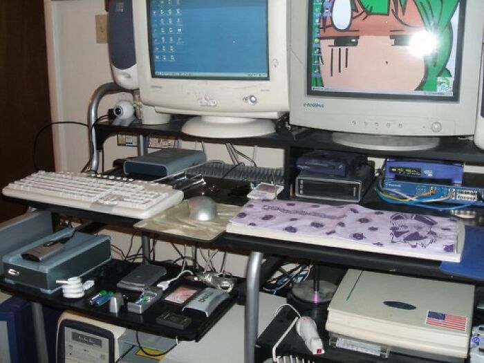 Old Internet setup with CRT monitors, a keyboard, and various vintage tech devices on a cluttered desk.