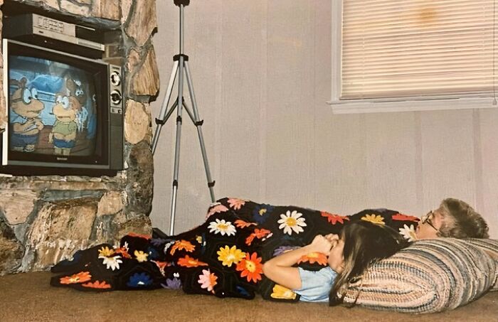 Kids watching cartoons on an old TV, wrapped in a floral blanket, evoking an old-internet feel.
