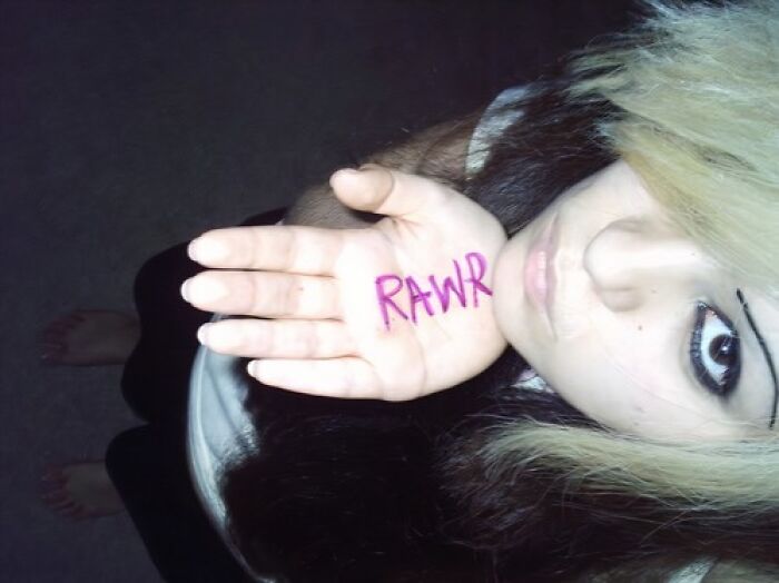 Young person with emo hairstyle holds up hand showing "RAWR" in pink, capturing old internet feel.