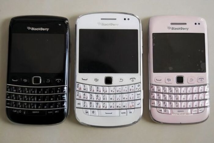 Three old BlackBerry phones, black, white, and pink, showcasing the classic QWERTY keyboard, evoke an old-internet feel.