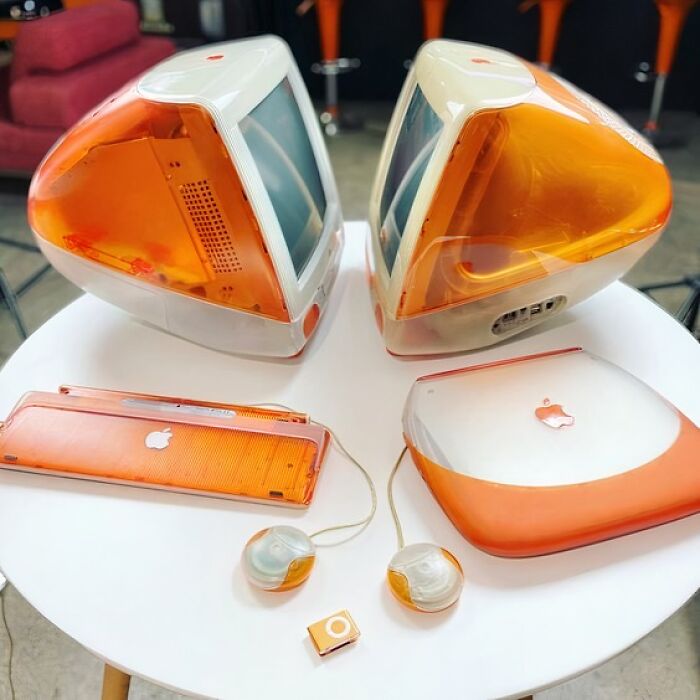 Retro-style iMacs and accessories in vibrant orange on a white table, evoking an old-internet feel.