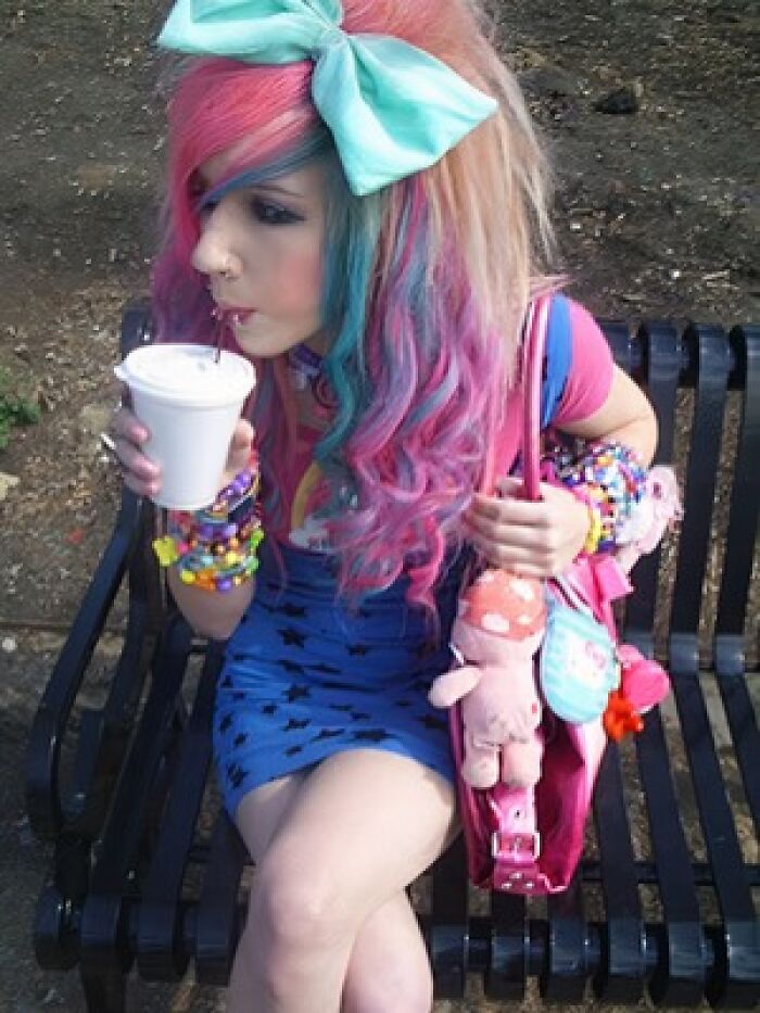 Young woman with colorful hair and 2000s fashion sipping a drink on a bench, exemplifying old-internet-feel aesthetics.