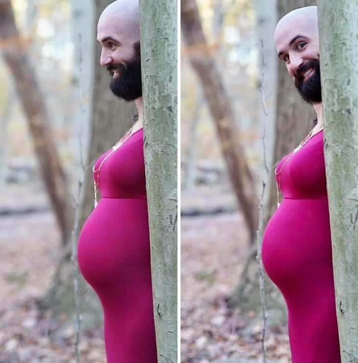 Man in a humorous pregnancy photo with a fake belly, smiling behind a tree in the woods.