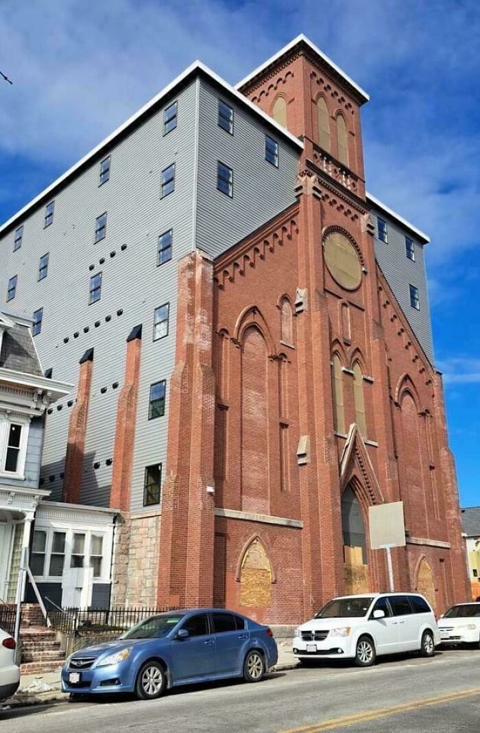 Unique bizarre building combining old brick church facade with modern grey siding in urban street setting under blue sky
