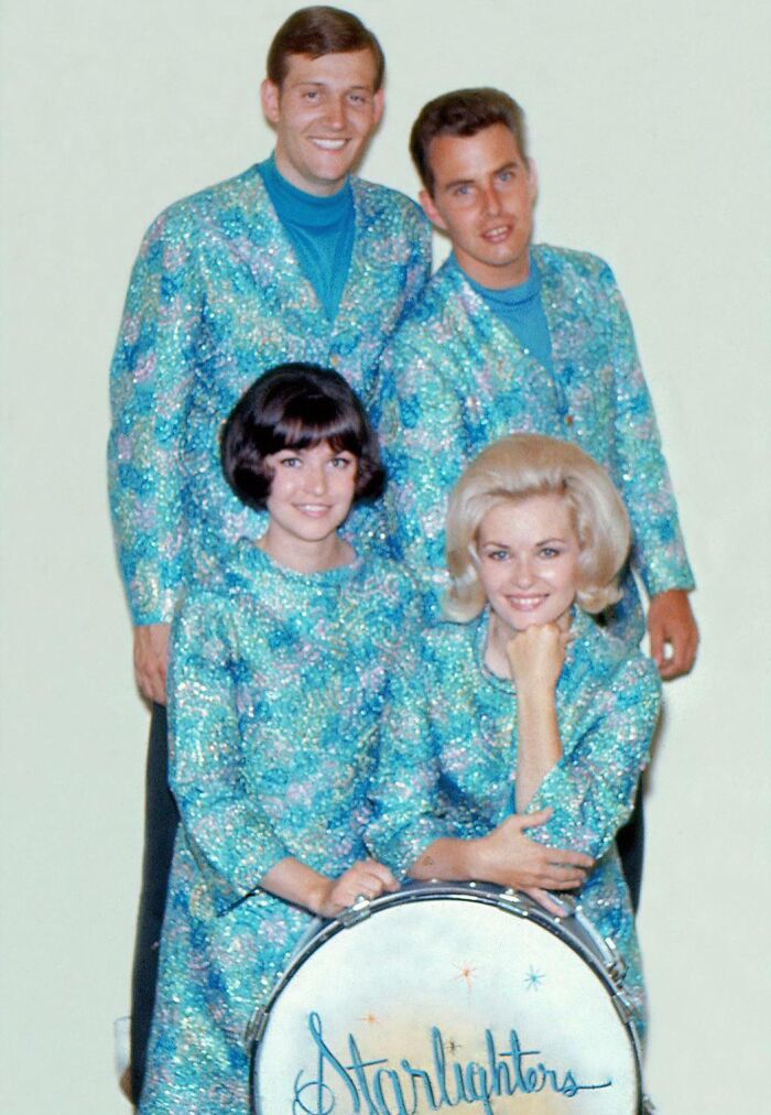 Four people in matching blue and green outfits from 60s fashion, standing and sitting around a drum that says "Starlighters."