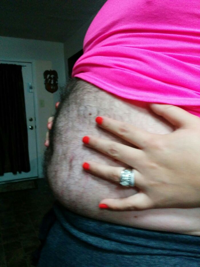 Hand with red nails on a hairy belly in a funny pregnancy situation.