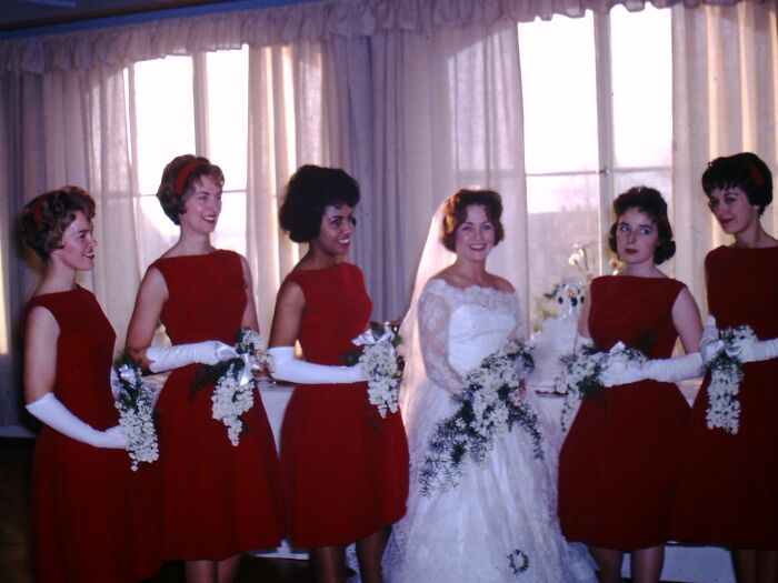 1960s fashion looks: bridal party in red dresses and white gloves, posing with the bride in a lace wedding gown.