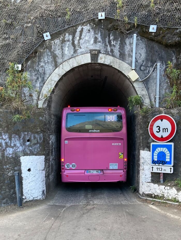 A pink bus squeezing through a narrow tunnel, illustrating a perfect fit.