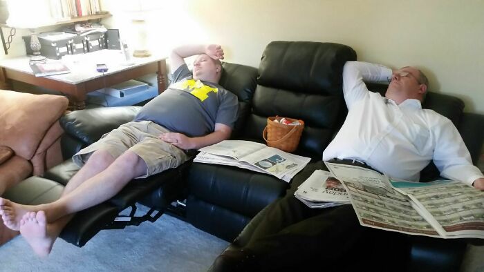 Two men sleeping on reclining sofas, surrounded by newspapers, illustrating funny pregnancy situations.