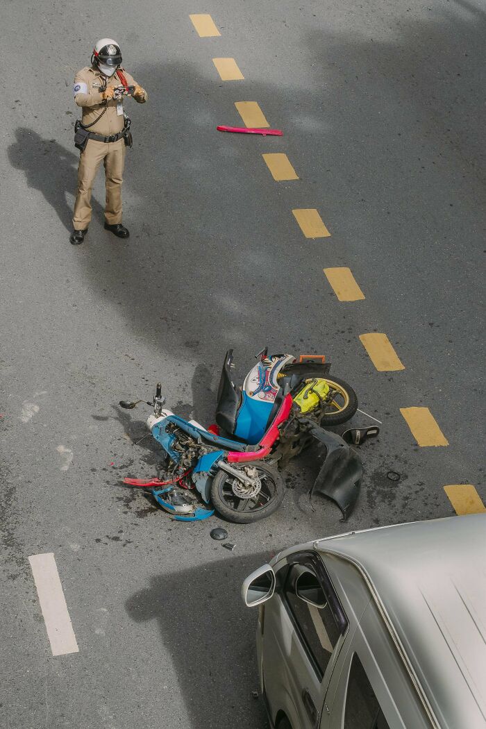 Motorcycle accident on city street captured in creative street photography, with a police officer documenting the scene.