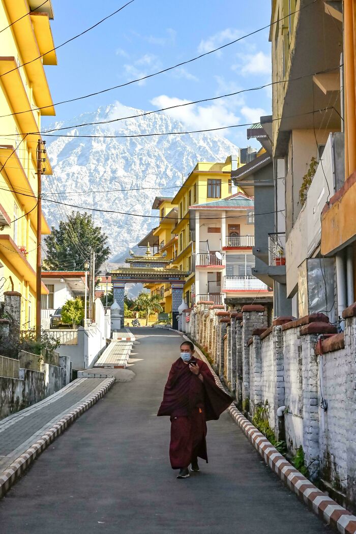 Monk in robe walks through vibrant street with mountain backdrop, showcasing creative street photography elements.