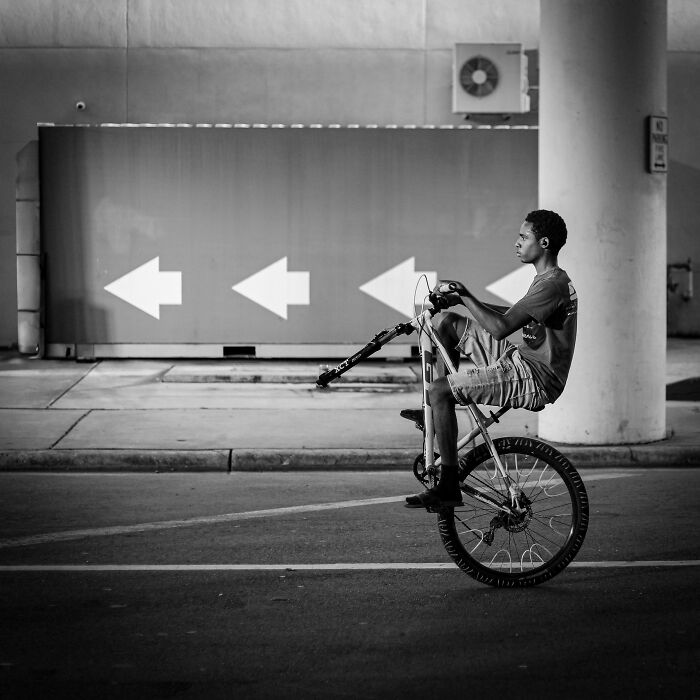 Young man performing a wheelie on a bicycle in urban setting, capturing the essence of creative street photography.