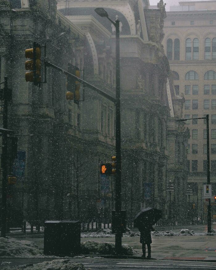 A person with an umbrella stands at a snowy urban intersection, showcasing creative street photography.