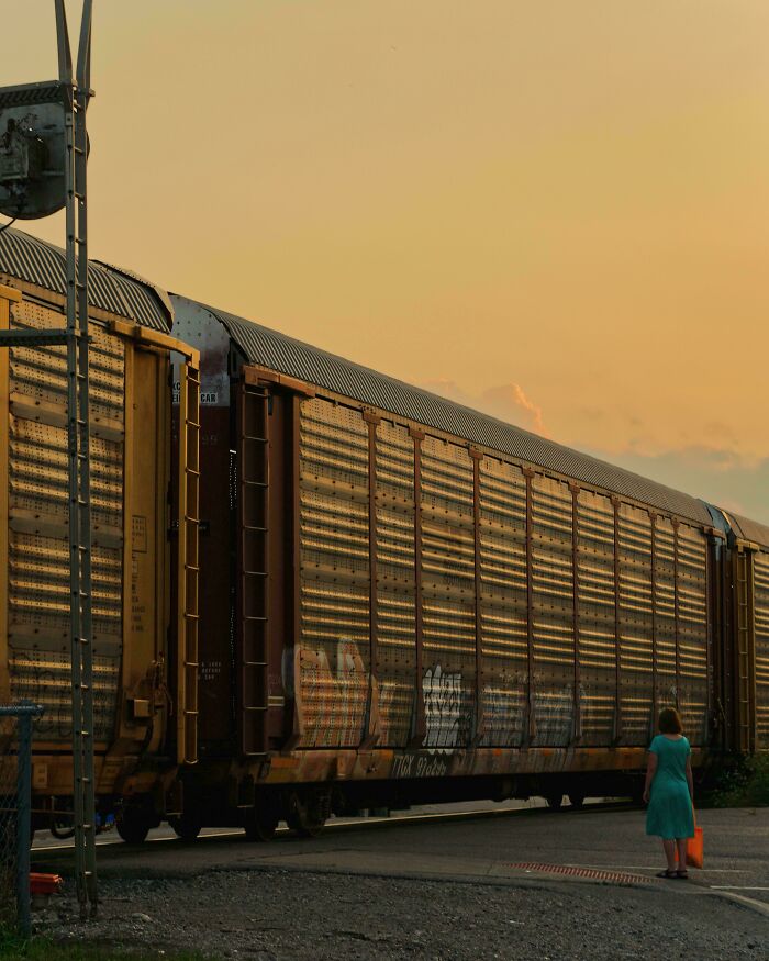 A woman in a turquoise dress stands by a graffiti-covered freight train at sunset, showcasing creative street photography.