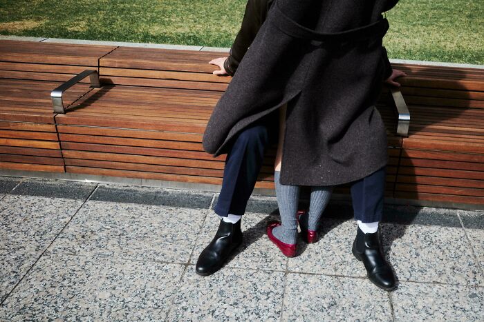 A unique moment captured in creative street photography shows a couple sitting closely on a wooden bench.