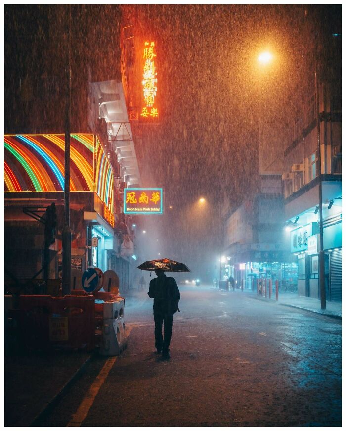 Nighttime street scene with neon lights, rain, and a person holding an umbrella, highlighting creative street photography.