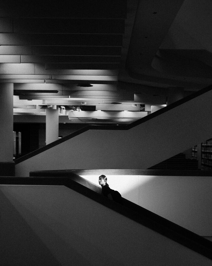 Black and white creative street photography of person on a modern staircase, with dramatic lighting and geometric shapes.