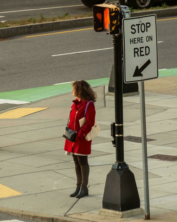 Person in a red coat standing by a "Stop Here on Red" sign at a crosswalk, capturing creative street photography.