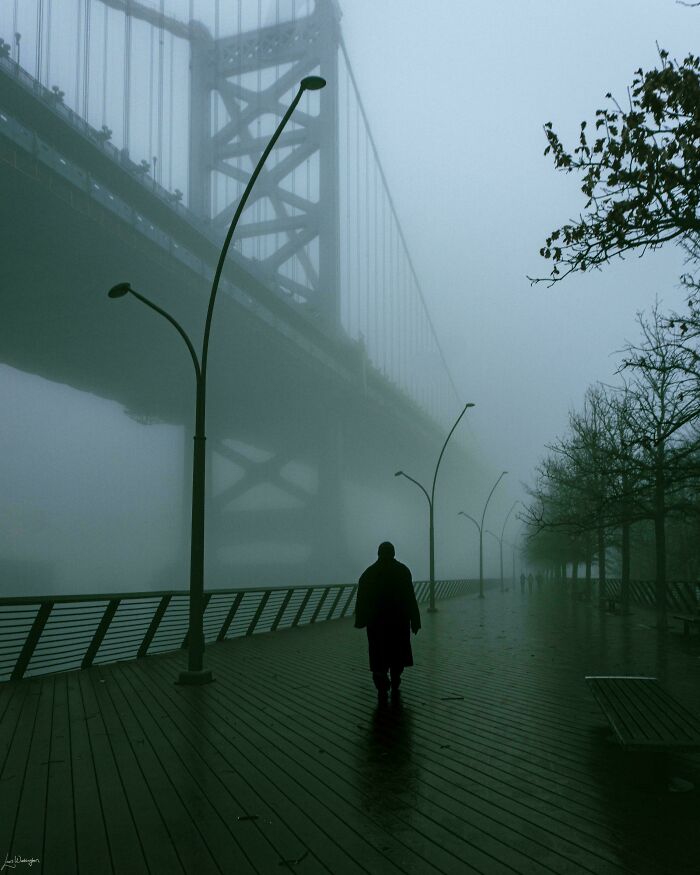 A solitary figure walks along a foggy boardwalk under a bridge, showcasing creative street photography.