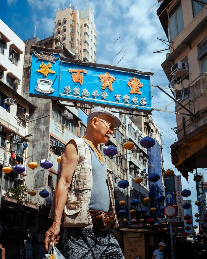 Elderly man walking in vibrant street with colorful lanterns and tall buildings, showcasing creative street photography.