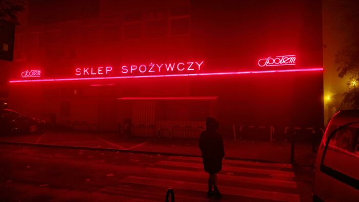 Person standing in front of a neon-lit store at night, capturing a moment of creative street photography.