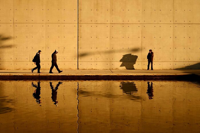 People walking by a wall with dramatic shadows and reflections on water, showcasing creative street photography elements.
