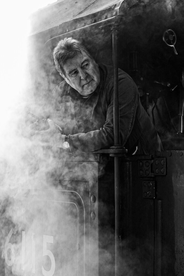 A creative street photography capture of a man leaning out of a train amid swirling smoke.