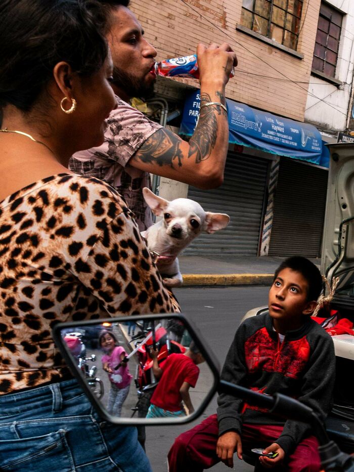 Street scene with a man drinking, a woman holding a dog, and a boy observing, capturing creative street photography vibes.