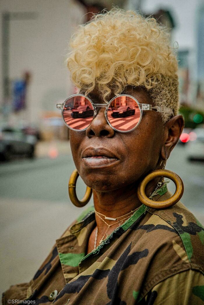 Person with blonde curly hair and reflective sunglasses, capturing urban life in creative street photography.