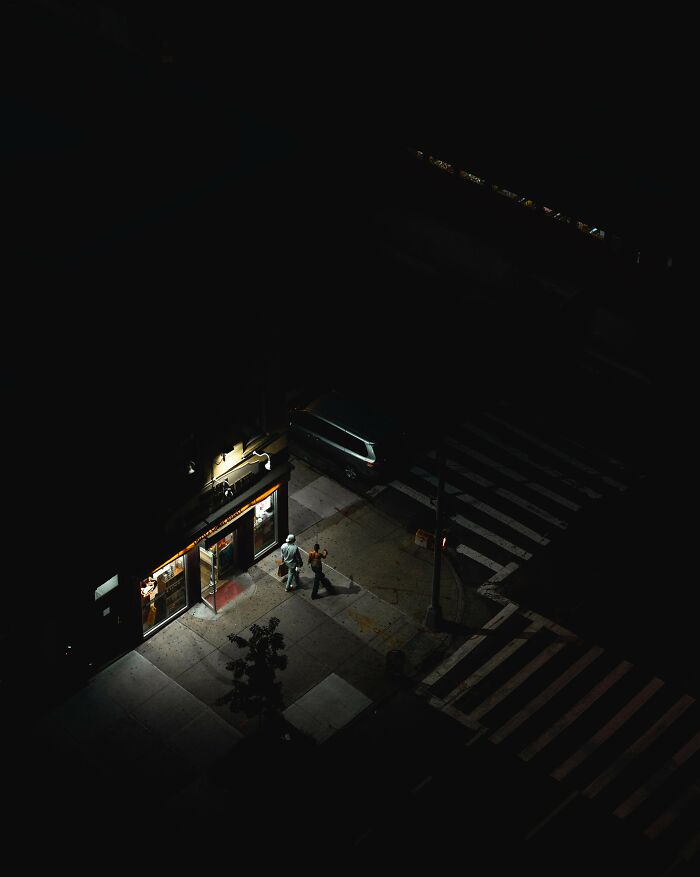 Creative street photography capturing a couple walking at night by an illuminated storefront.