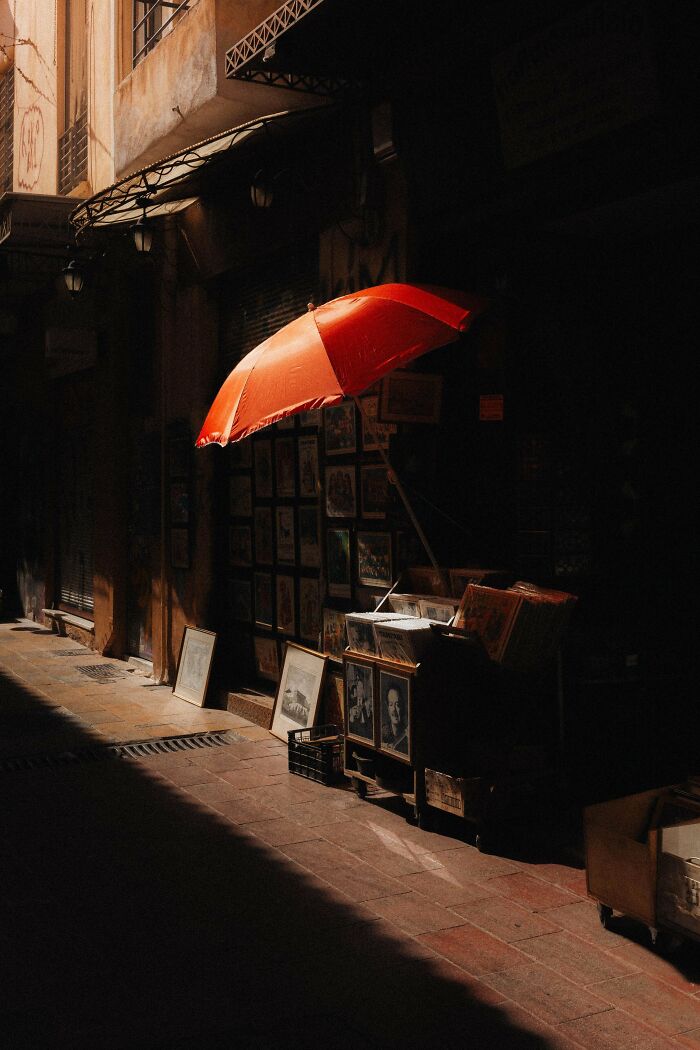 Creative street photography of a narrow alley with an orange umbrella and vintage art displayed on the walls.