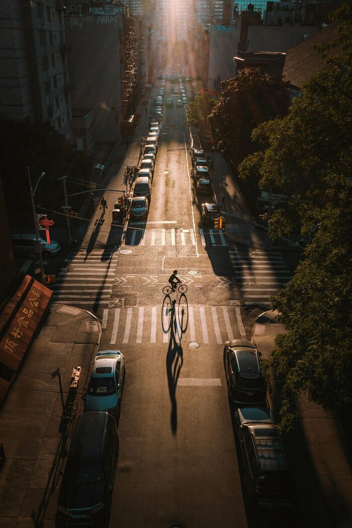 Biker casting long shadow on sunlit street, showcasing creative street photography.