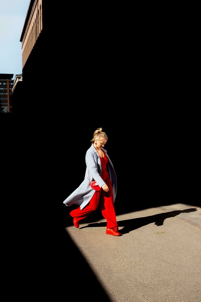 Person in a bright red outfit and gray coat walking confidently through stark shadows, embodying creative street photography.