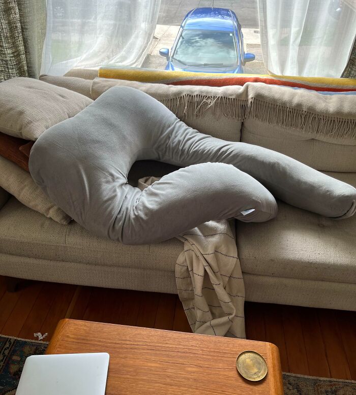 Pregnancy pillow humorously shaped like a person sitting on a couch, funny situation in living room.