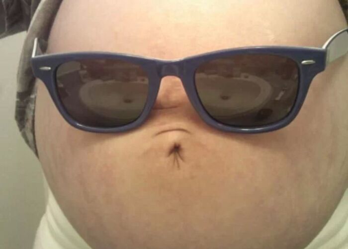 Pregnant belly wearing sunglasses creating a funny face illusion.